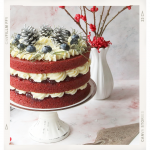 A red velvet cake with three tiers and cream frosting sits on a cake stand, next to a vase containing sticks with red berries on them.