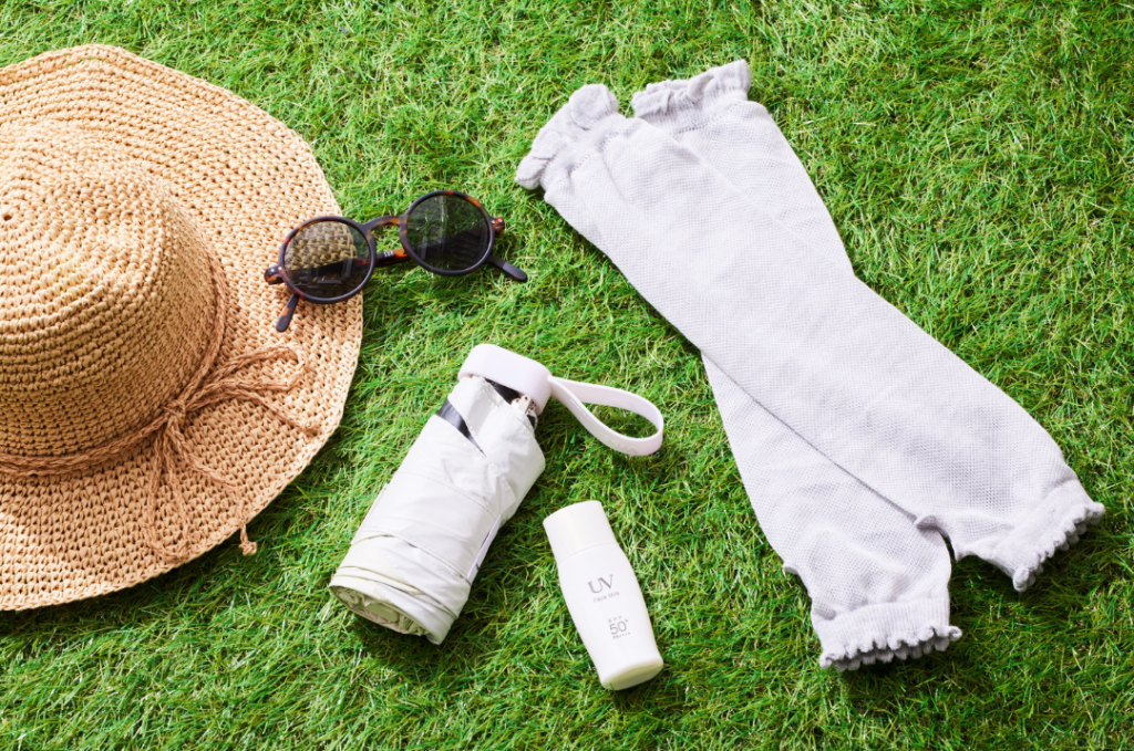 Sun hat, sunglasses, sunscreen, protective arm coverings, and an umbrella laid out on grass.