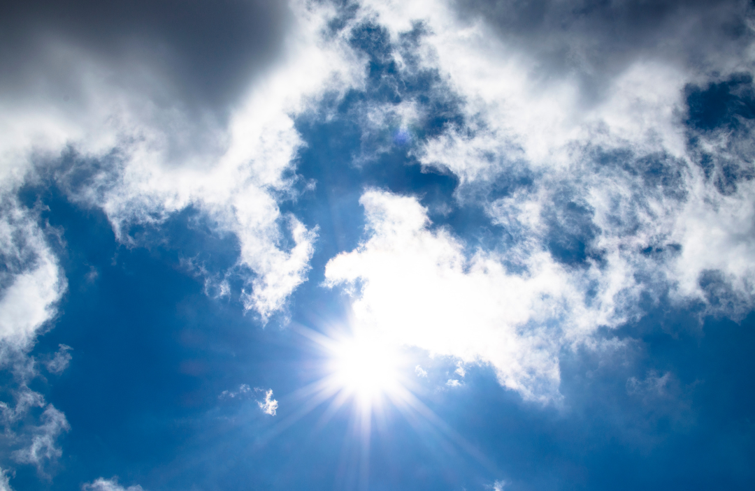Sun shining through a gap in clouds against a blue sky.