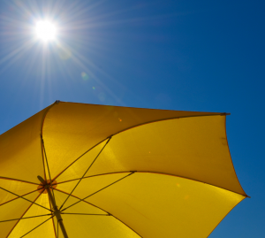 Large yellow parasol against a clear blue sky with sun shining overhead.